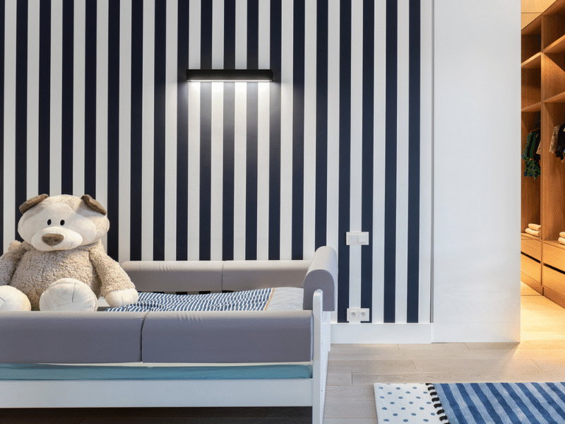 a striped accent wall in a child's room with a giant teddy bear on the bed